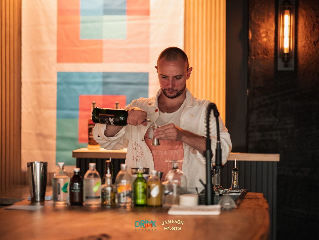 Photo of bartender pouring Scotch into a jigger. Dim light.